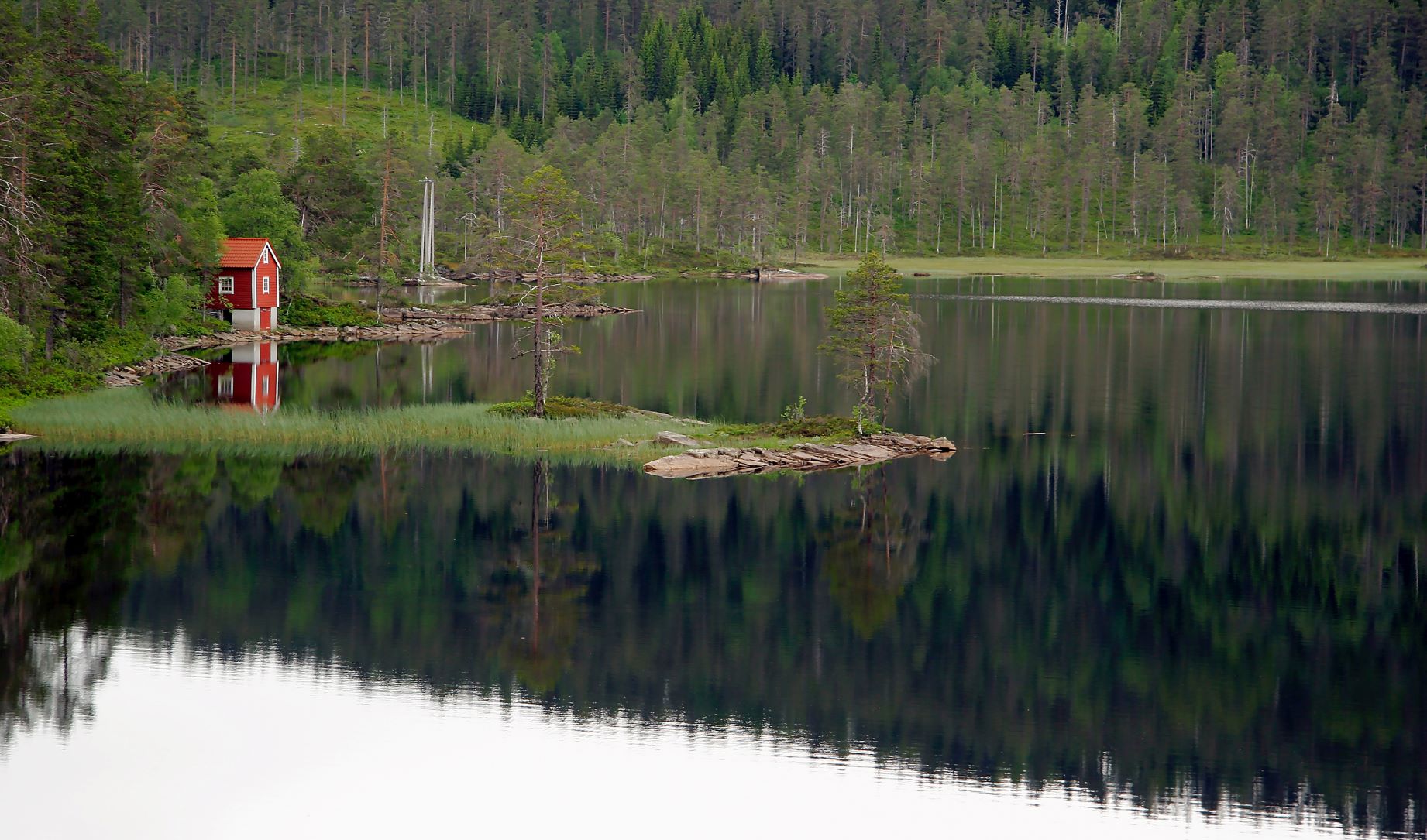 En liten röd stuga vid en strand med spegelblank sjö